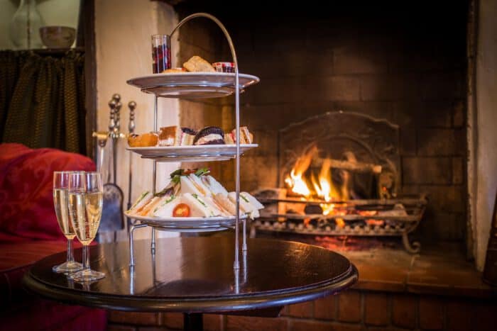 Cozy afternoon tea setup with sandwiches, pastries, and champagne near a warm fireplace at Marston F.
